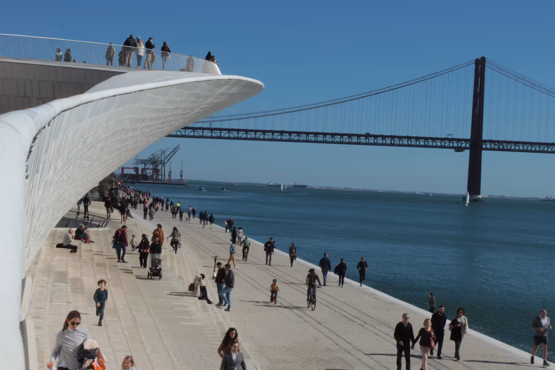 Tourists and cyclists enjoy the scenic Belém waterfront promenade with the 25 de Abril Bridge on the Lisbon e-bike tour