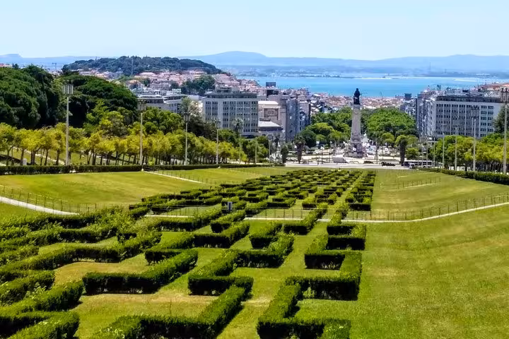 View from Eduardo VII Park in Lisbon showcasing manicured hedges, cityscape, and distant Tagus River on a sunny day.