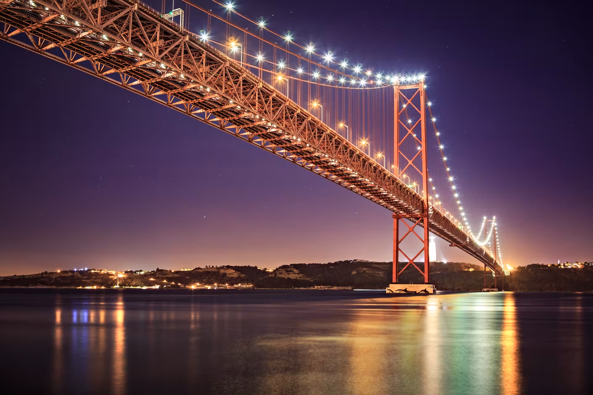 Illuminated 25 de Abril Bridge over the Tagus River at night, a highlight of Lisbon's Fado Night Tour.