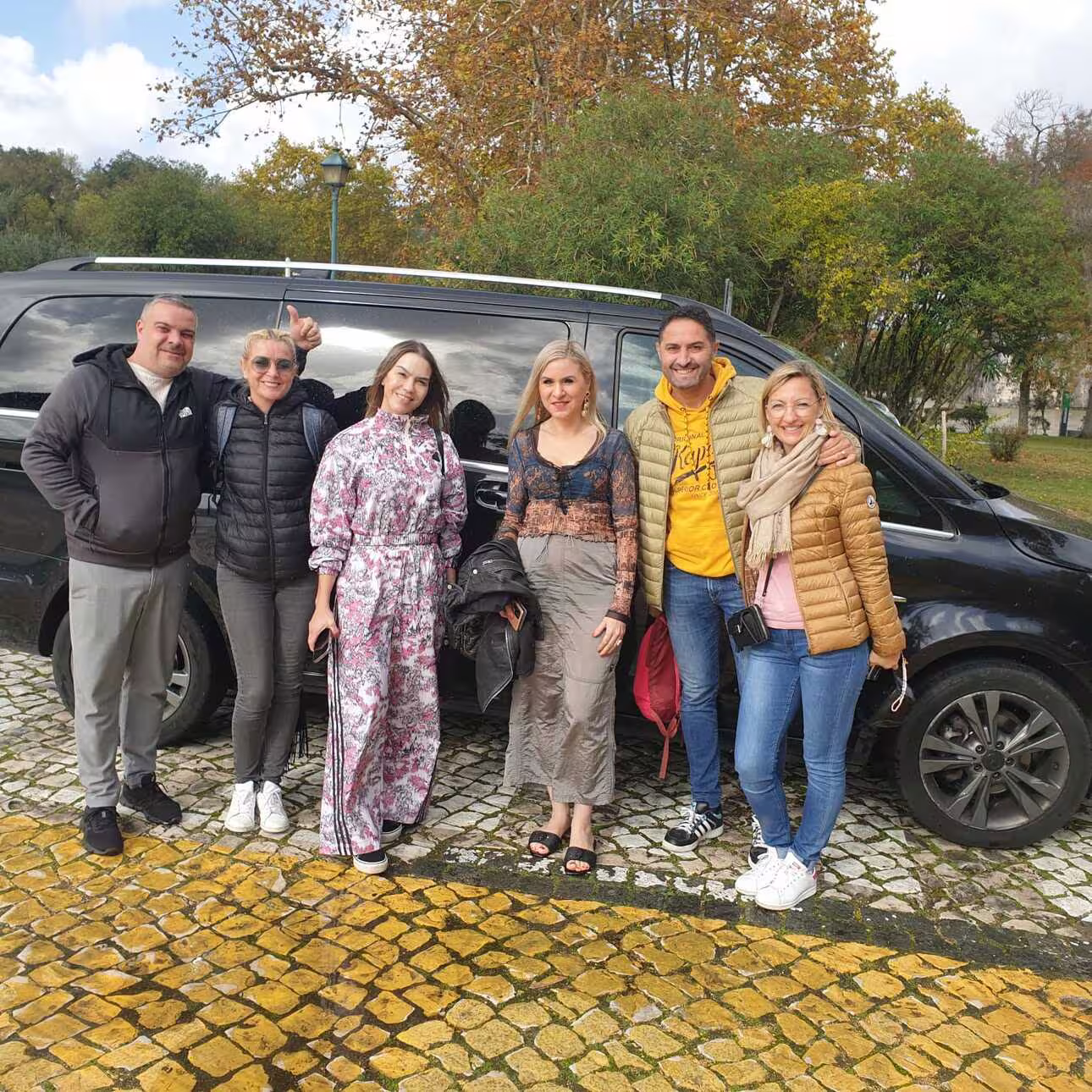 Tour group poses by a van, ready to explore the highlights of Fátima, Nazaré, Batalha, and Óbidos from Lisbon.