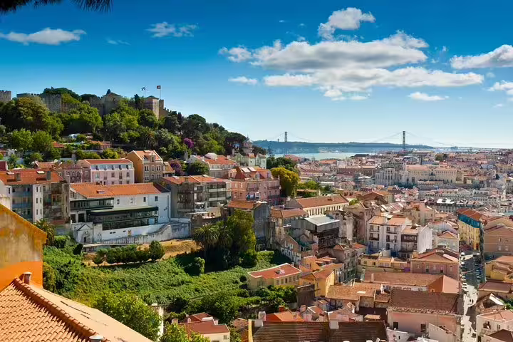 Scenic view of Lisbon's historic rooftops and the 25 de Abril Bridge on a sunny day, perfect for a private Lisbon and Fatima tour.