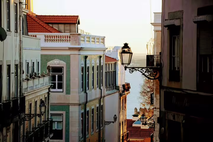 Charming Lisbon street view with historic tiled buildings and vintage lanterns, overlooking the Tagus River at sunset.