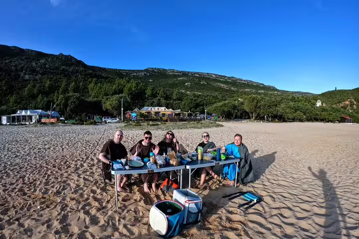 Group enjoying a seaside lunch on a sandy beach during Lisbon's full-day kayak and coasteering adventure.