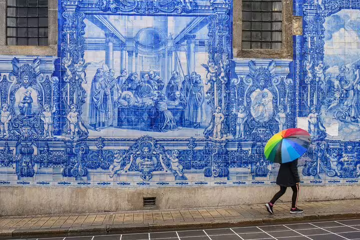 Person with colorful umbrella walks past intricate blue azulejo tiles on a hidden Lisbon street during a local private tour.
