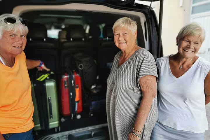 Three smiling travelers standing by their luggage loaded in a van, ready for a private transfer from Lisbon to Madrid with stops in Evora and Toledo.