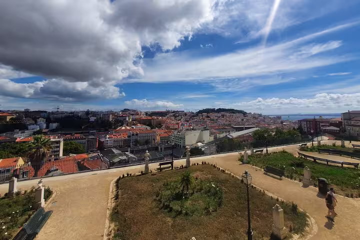 Scenic view of Lisbon's historic old town with red rooftops, lush gardens, and blue skies, perfect for a half-day tour exploration.