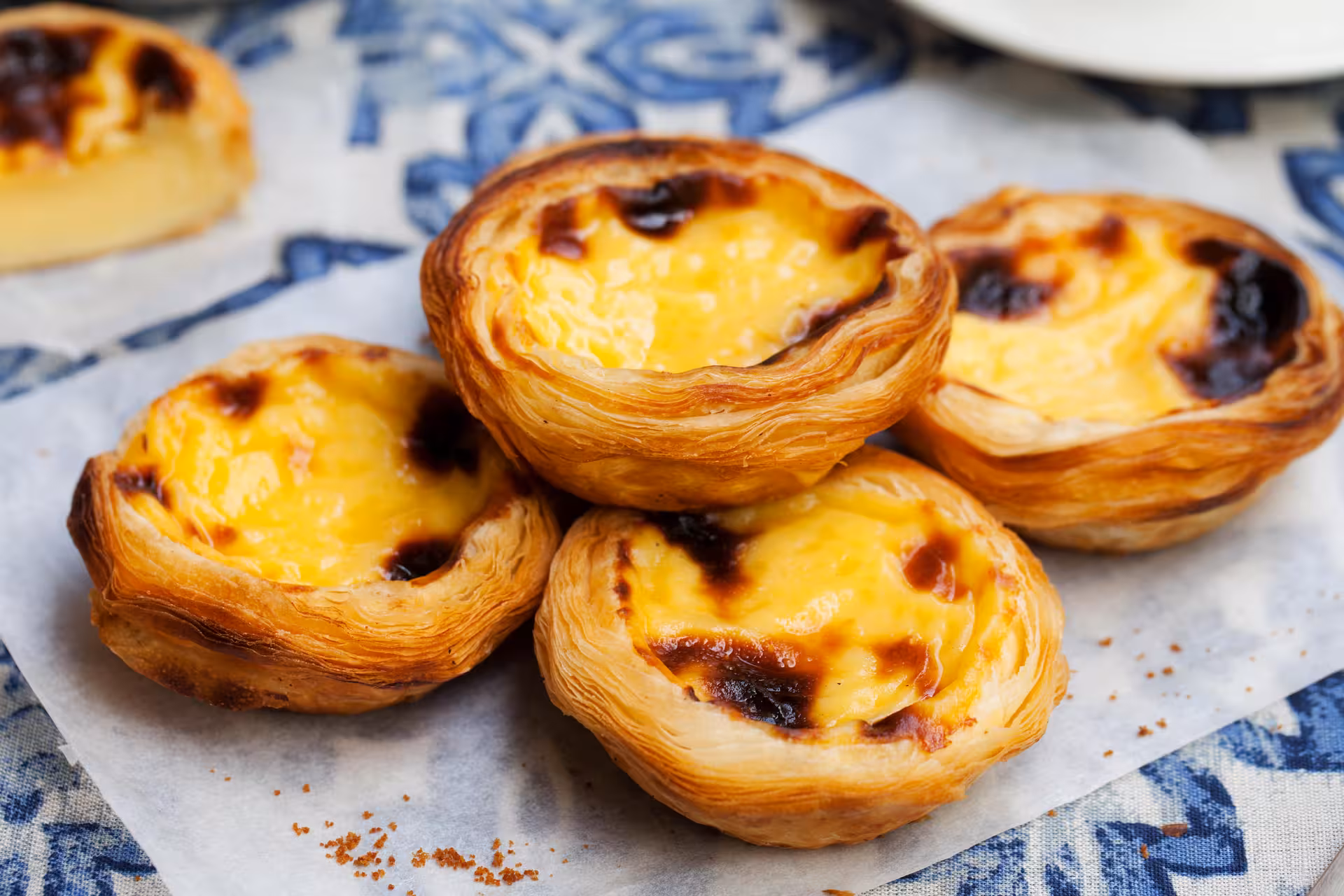 Close-up of traditional Portuguese egg tarts, Pastéis de Nata, on a decorative blue and white tile background.
