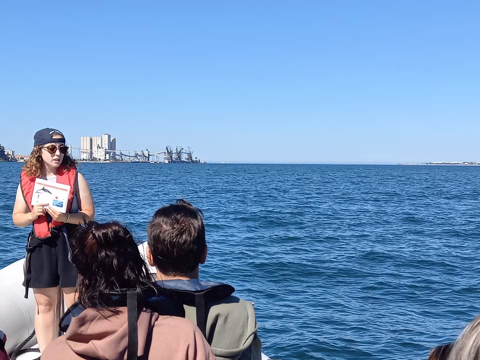 Guide briefs passengers on Lisbon plastic pickup & boat tour, cruising the Tagus River with waterfront views