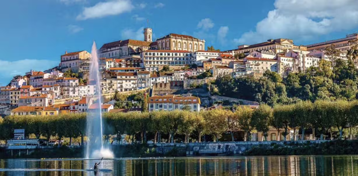 Scenic view of Coimbra's historic skyline with a fountain on the Mondego River, en route from Lisbon to Porto.