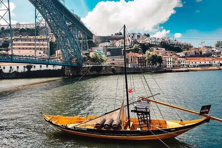 Traditional rabelo boat on the Douro River with Porto cityscape and Dom Luís I Bridge, highlighting the Lisbon to Porto tour.