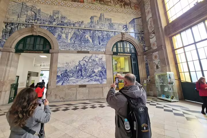 Travelers photographing the iconic blue azulejos at São Bento Railway Station in Porto on a 3-day Lisbon to Douro Valley tour.