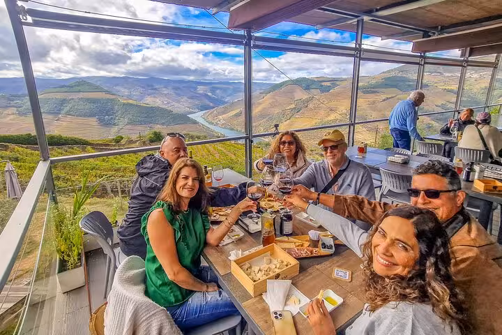 Friends toast Douro Valley wine at scenic terrace stop on Lisbon to Porto ride, overlooking river vineyards