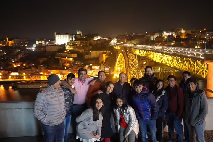 A group enjoying a night view of Porto's illuminated Dom Luís I Bridge during a private 2-day tour from Lisbon to Porto.