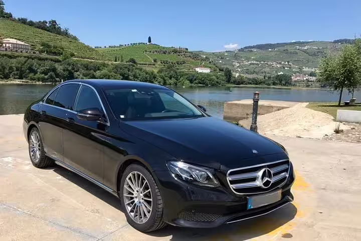 Luxury black sedan parked by scenic Douro River vineyards for Lisbon to Porto private journey with customizable stops.