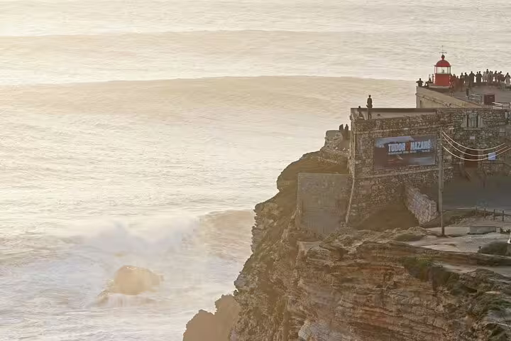 Sunlit cliffside with iconic lighthouse at Nazaré, a must-see on the Lisbon to Porto private transfer journey.
