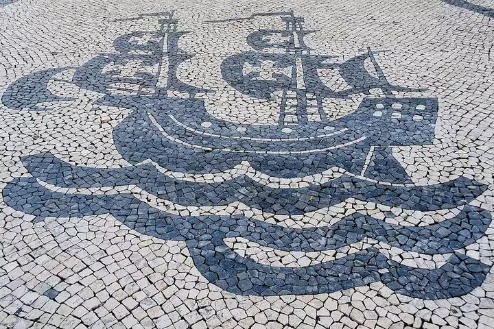 Traditional Portuguese mosaic of a ship on cobblestone pavement in Lisbon, showcasing local art and history on a full-day tour.