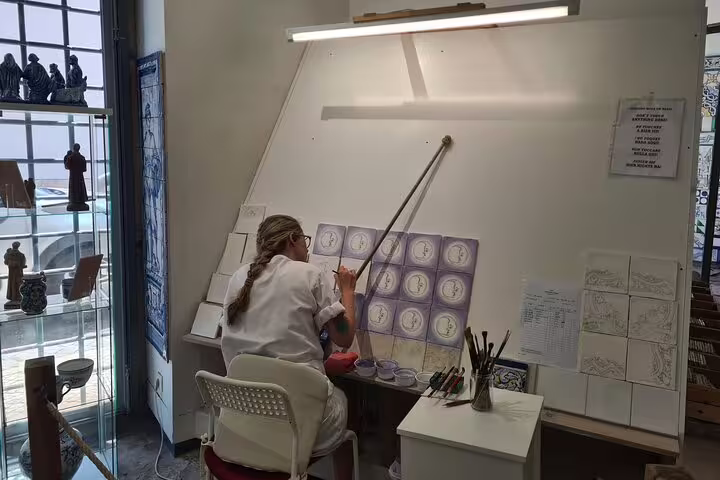 Artist painting traditional Portuguese tiles in a Lisbon studio, featured on a private TukTuk tour with a local guide.