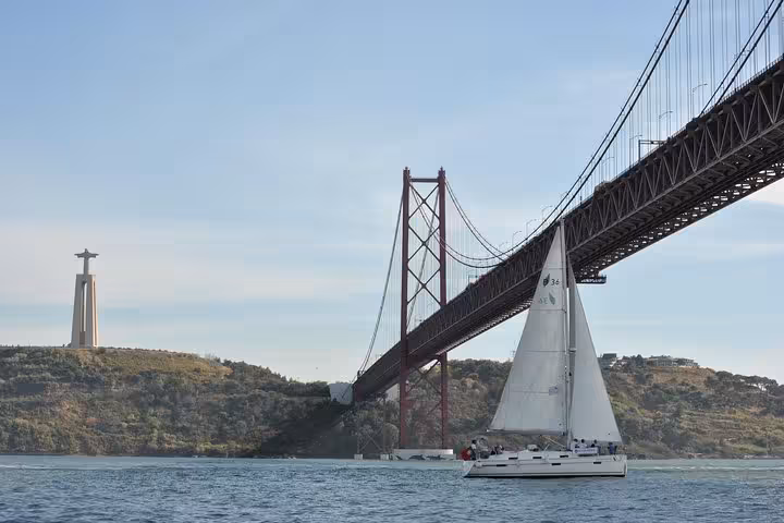 Sailboat on Lisbon private sailing cruise passing 25 de Abril Bridge and Cristo Rei, drink included
