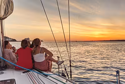 Friends enjoying a breathtaking golden sunset view from the deck of a private sailing cruise in Lisbon