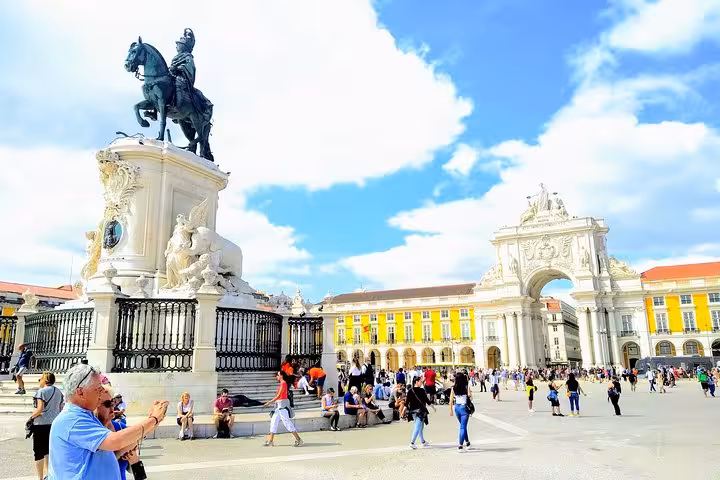 Tourists admire Praça do Comércio's statue and Arco da Rua Augusta on a sunny day in Lisbon city center.