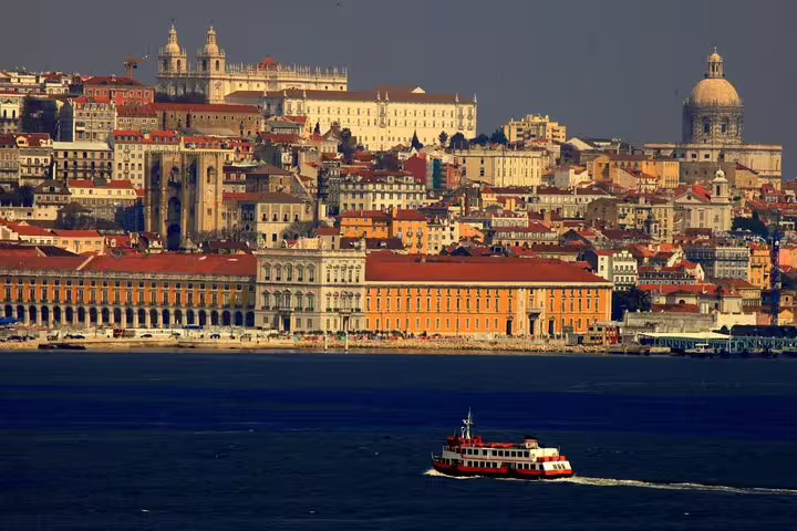Scenic view of Lisbon's historic cityscape with a boat on the Tagus River, ideal for a half-day private tour in a premium vehicle.