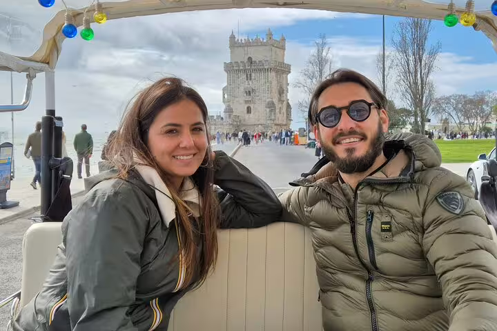 Couple enjoying a private TukTuk tour with a local guide in Lisbon, with the iconic Belém Tower in the background.