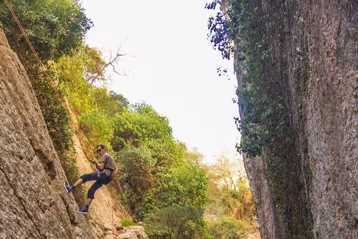 Adventurer rappelling down a rocky cliff surrounded by lush greenery on a rock climbing trail near Lisbon.