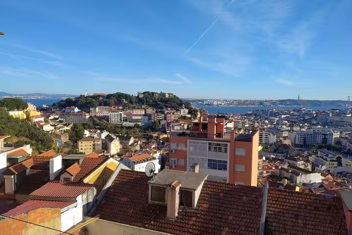 Panoramic view of Lisbon's vibrant rooftops and the historic São Jorge Castle against a clear blue sky.