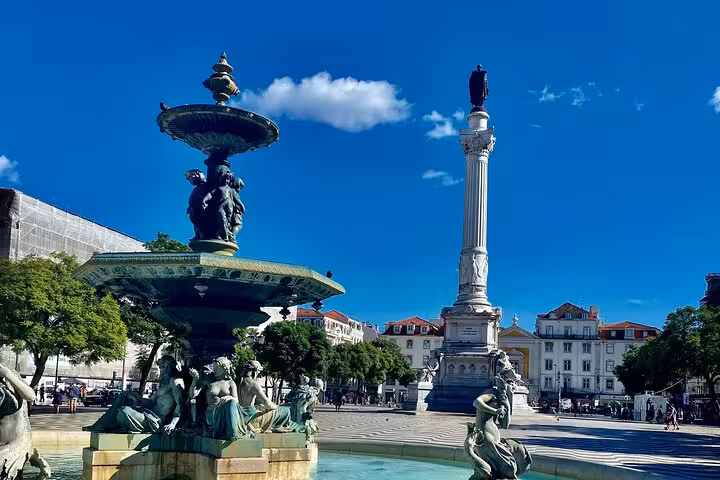 Majestic Rossio Square fountain and column under a clear blue sky in Lisbon's vibrant city center.
