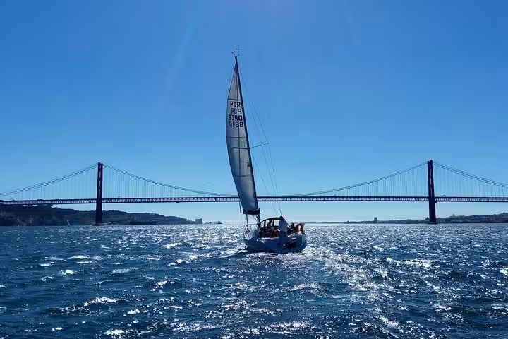 Private Lisbon sailing yacht cruise on the Tagus River passing under the 25 de Abril Bridge at sunset