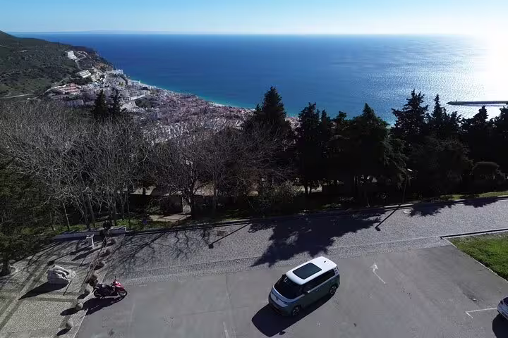 Aerial view of an Electric ID Buzz driving along the scenic Lisbon coast towards Sesimbra, overlooking the ocean.