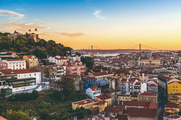 Scenic view of Lisbon's historic skyline at sunset, featuring São Jorge Castle and the 25 de Abril Bridge on a journey to Seville.