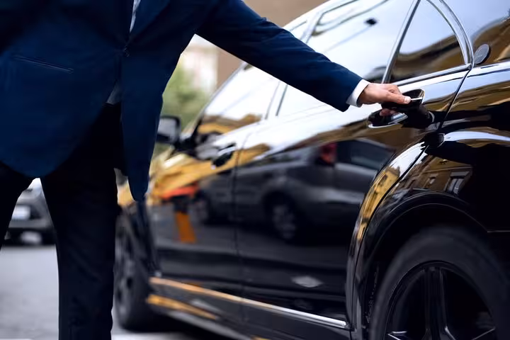 Chauffeur opening a sleek black Mercedes door for a Lisbon to Seville private transfer service.