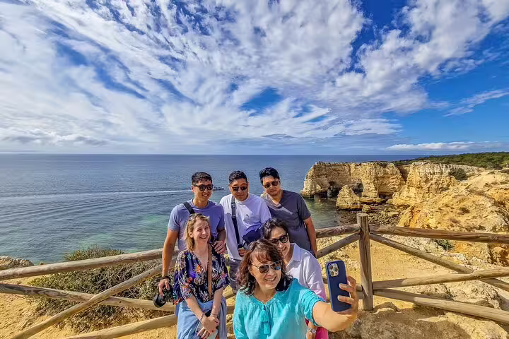 Group enjoying scenic Algarve coastline during Lisbon to Seville private transfer, capturing memories with ocean cliffs backdrop.