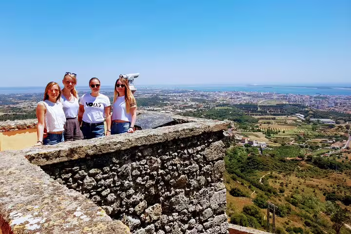 Group enjoying panoramic views of Lisbon's south coast from a historic stone terrace during a wine tour under a clear blue sky.