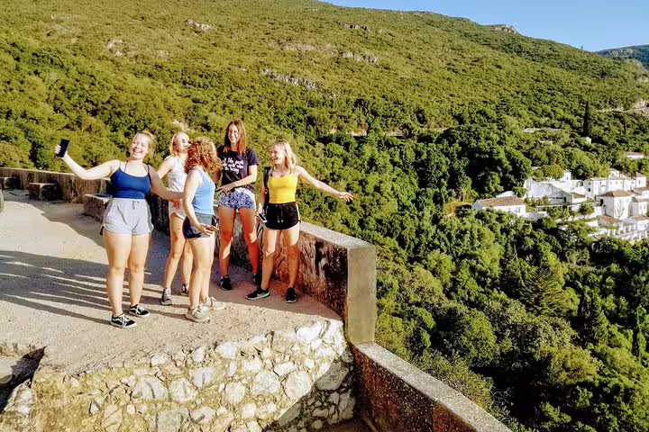 Group of friends enjoying panoramic views of lush green hills and white village during Lisbon's South Sights & Wine tour.