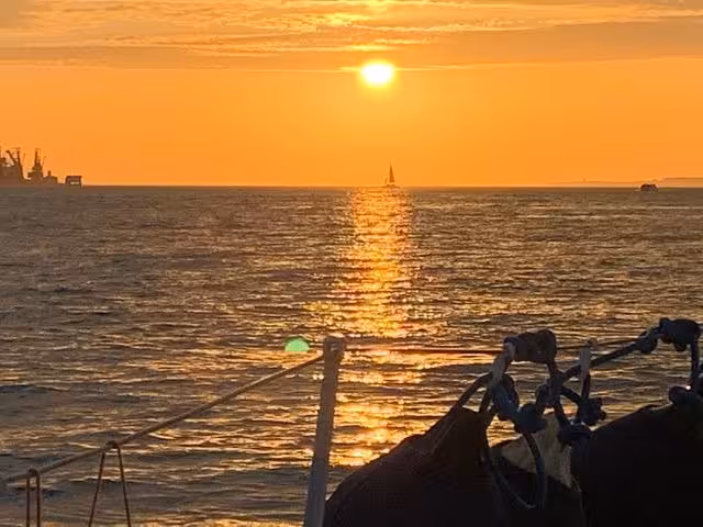Golden sunset over the Tagus River from a Lisbon boat tour, calm sea glow and distant sailboat