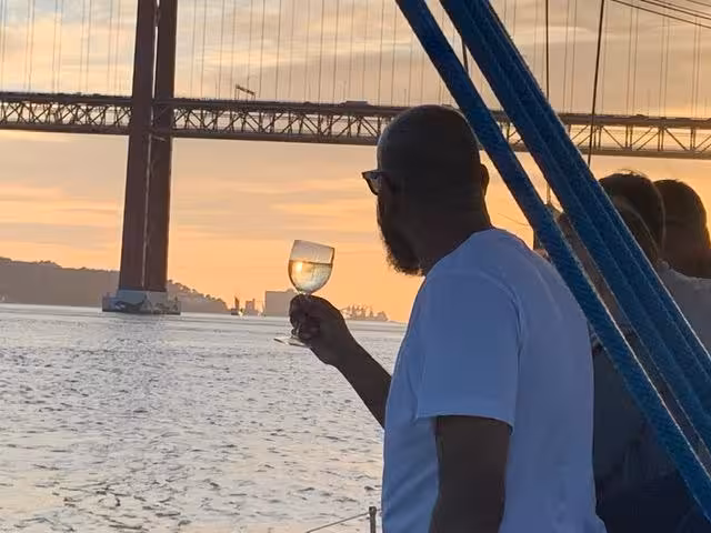 Guest toasts with wine on Lisbon sunset boat tour beneath 25 de Abril Bridge on the Tagus River