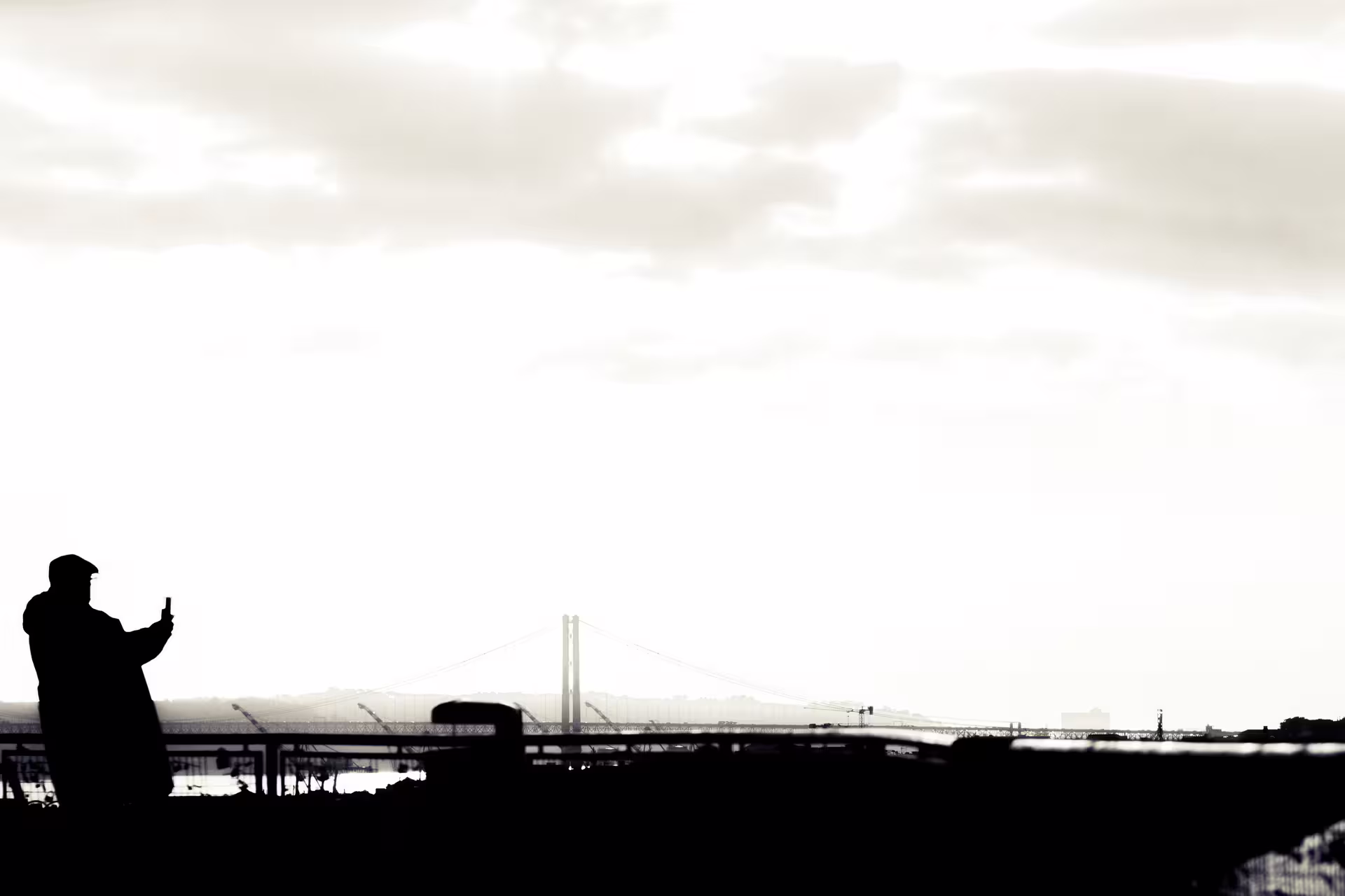 Silhouette of a person taking a photo at sunset with Lisbon's iconic bridge in the background, perfect for a Christmas lights tour.