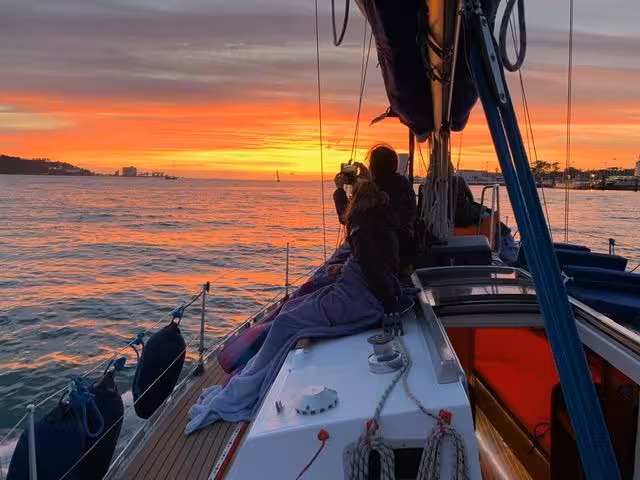 Guests relaxing on a sailboat at sunset in Lisbon, Tagus River cruise with wine and skyline views