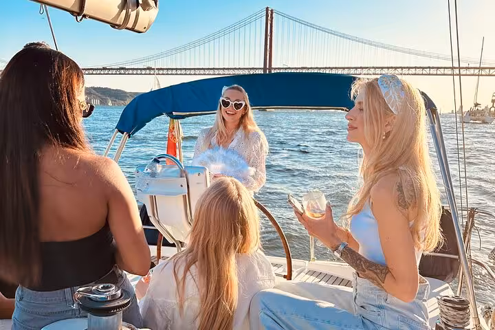 Sunset sailing on the Tagus River with friends and drinks, passing under the 25 de Abril Bridge in Lisbon