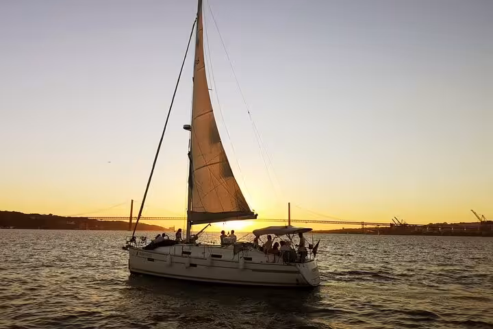 Private sailboat gliding on the Tagus River at golden sunset with Lisbon's 25 de Abril Bridge backdrop