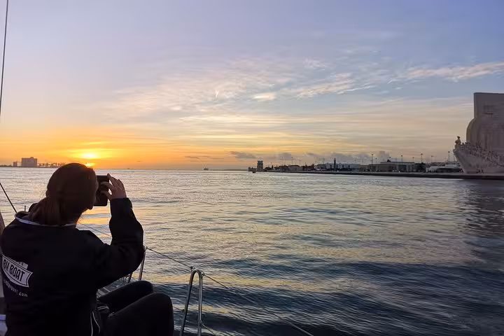 Lisbon sunset yacht cruise on Tagus River with guest watching golden sky near Belem waterfront on sailing tour