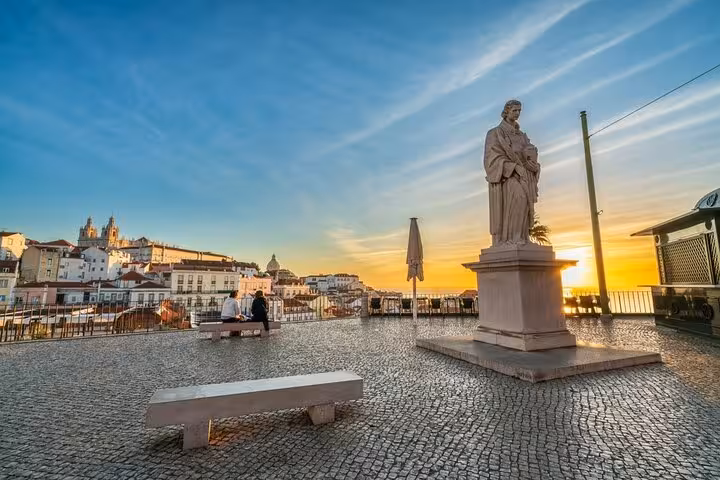 Sunset view at a Lisbon terrace with a statue, overlooking historic buildings and vibrant sky.