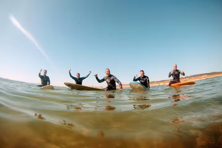 Group of surfers enjoying the Lisbon Surf Experience on clear waters, perfect for beginners and adventure seekers alike.