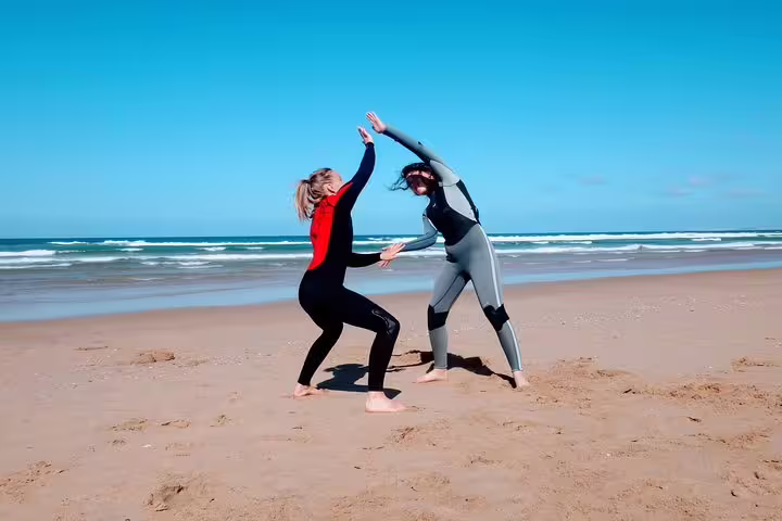 Two surfers in wetsuits practicing balance on a sunny Lisbon beach, perfect for a fun and adventurous surf experience.