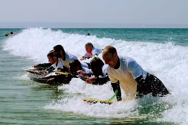 Group of surfers catching waves in Lisbon's sunny waters, perfect for a surf and wine adventure tour experience.