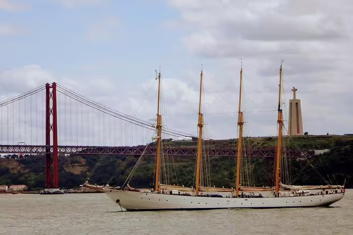 Majestic sailboat on the Tagus River with Lisbon’s iconic 25 de Abril Bridge and Cristo Rei statue in the background.