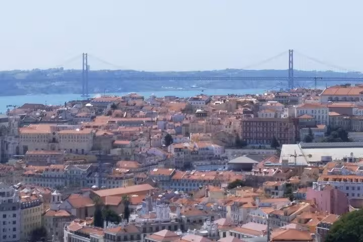 Scenic view of Lisbon's terracotta rooftops and the 25 de Abril Bridge over the Tagus River in the background.