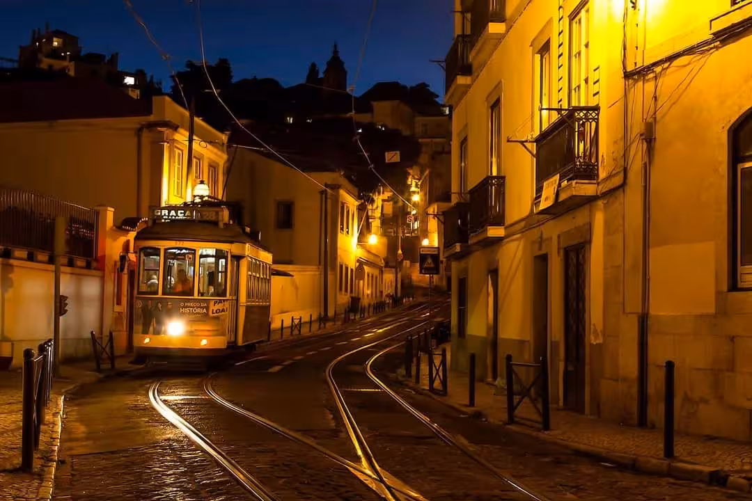 Classic Lisbon yellow Tram 28 at night on Alfama street, cobblestone tracks and warm city lights